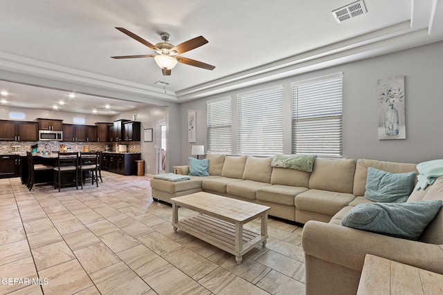 living room featuring ceiling fan, visible vents, and a raised ceiling