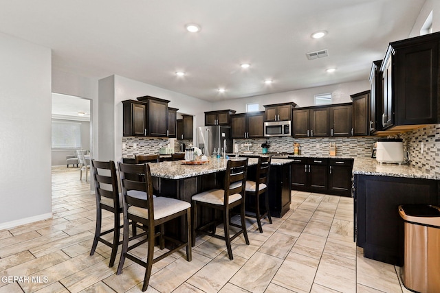 kitchen featuring light stone counters, appliances with stainless steel finishes, an island with sink, and decorative backsplash
