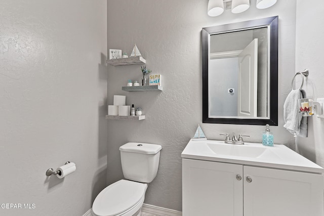 bathroom featuring baseboards, a textured wall, toilet, and vanity