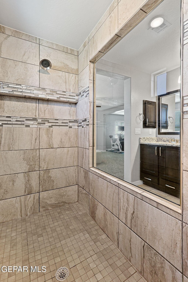 full bath with a tile shower, visible vents, and vanity