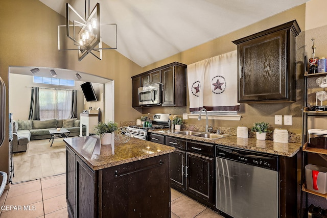 kitchen with dark brown cabinetry, a kitchen island, appliances with stainless steel finishes, dark stone countertops, and a sink