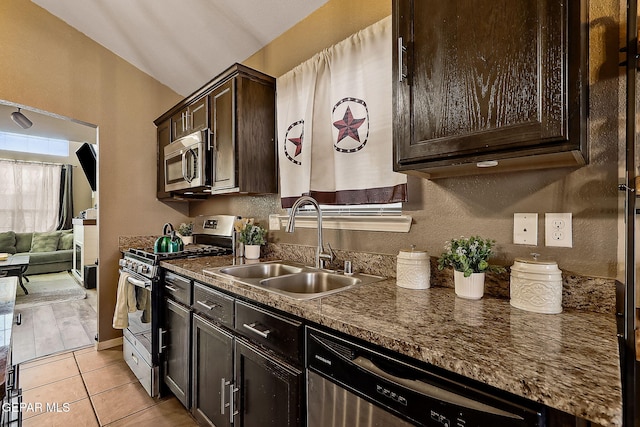 kitchen with light tile patterned floors, dark brown cabinetry, stainless steel appliances, a sink, and dark stone counters