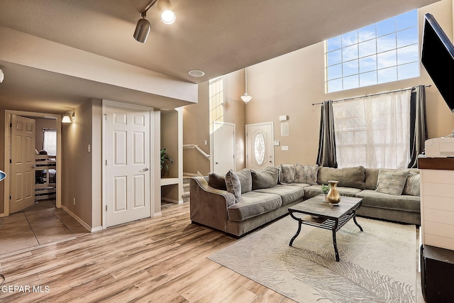 living room with light wood-style flooring, a high ceiling, baseboards, stairway, and rail lighting