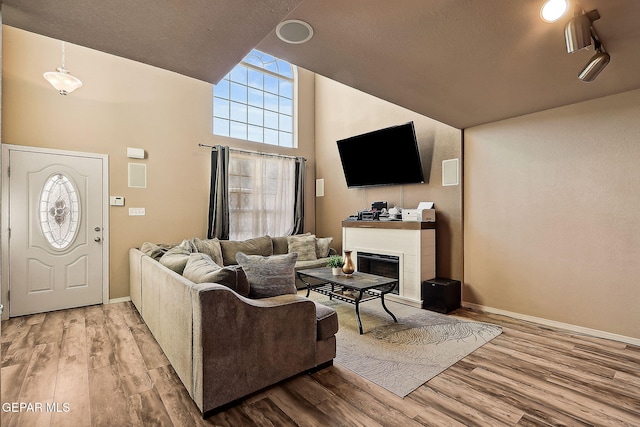 living area featuring light wood finished floors, baseboards, high vaulted ceiling, and a glass covered fireplace