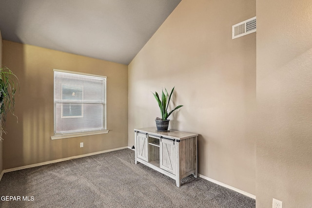 empty room featuring vaulted ceiling, dark carpet, visible vents, and baseboards