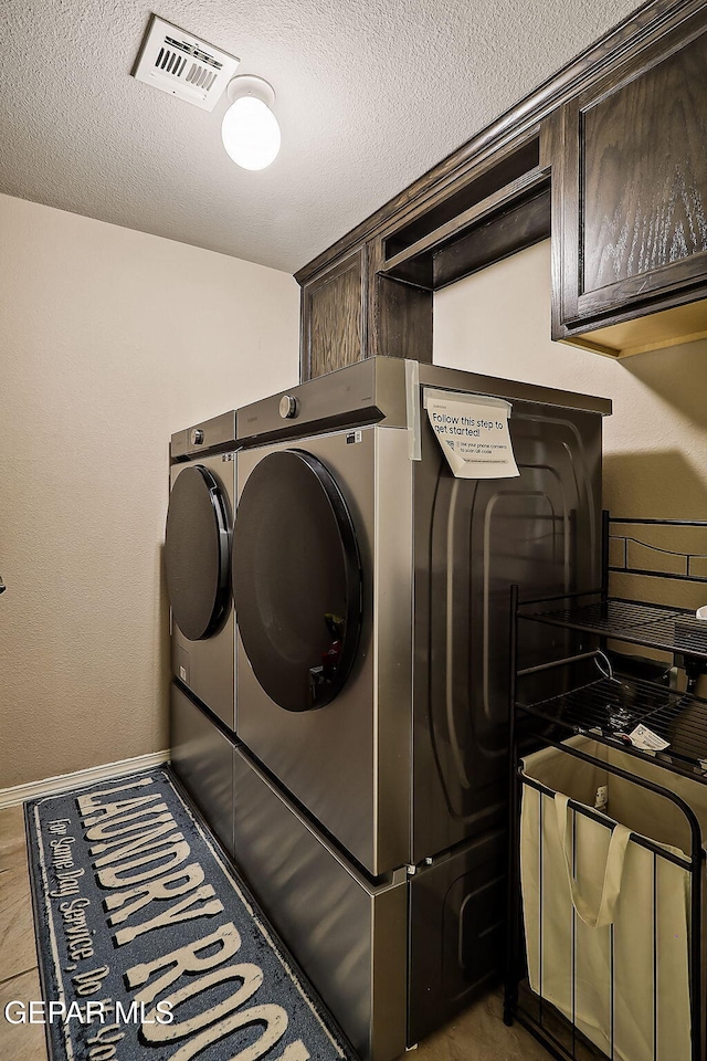 laundry area featuring cabinet space, visible vents, a textured ceiling, separate washer and dryer, and baseboards