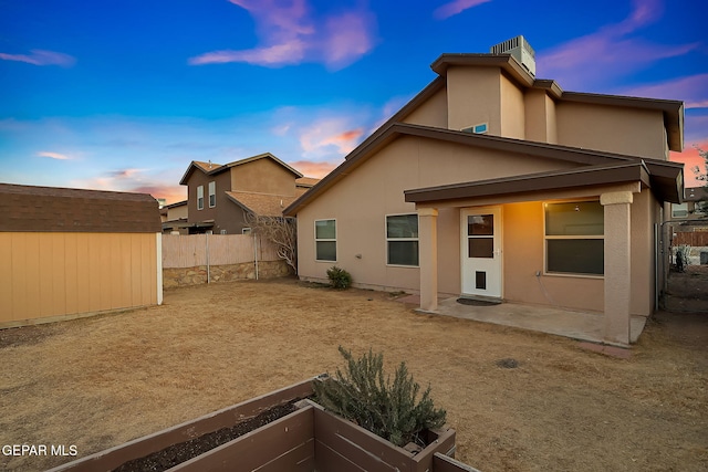 back of property at dusk with a storage shed, a patio, a fenced backyard, and stucco siding