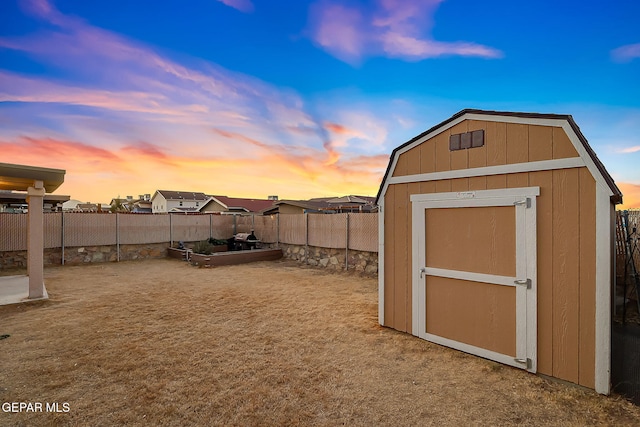 outdoor structure at dusk featuring a storage shed, an outdoor structure, and a fenced backyard