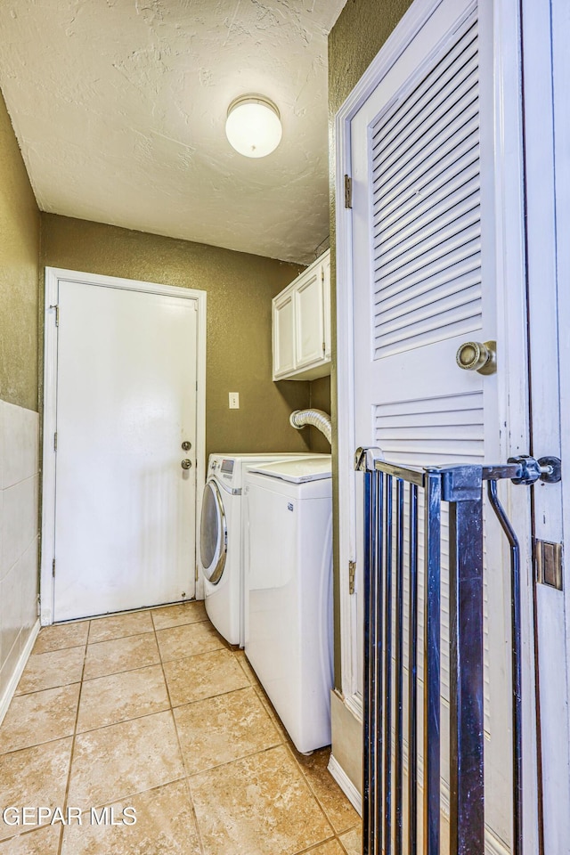 laundry area with light tile patterned floors, a textured wall, a textured ceiling, separate washer and dryer, and cabinet space