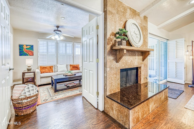 living area featuring dark wood-style floors, a fireplace, lofted ceiling with beams, ceiling fan, and a textured ceiling