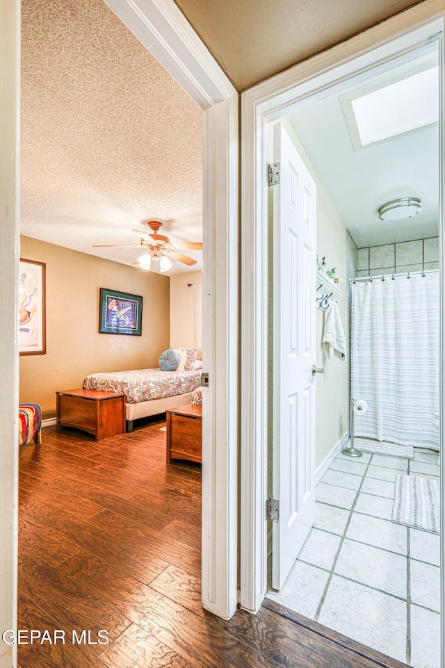 corridor featuring a skylight, a textured ceiling, baseboards, and wood finished floors