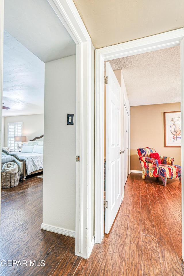 corridor featuring dark wood-style flooring, a textured ceiling, and baseboards