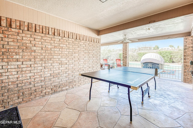 recreation room featuring stone flooring, ceiling fan, a textured ceiling, and brick wall