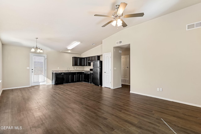 unfurnished living room with ceiling fan with notable chandelier, dark wood-style flooring, visible vents, baseboards, and vaulted ceiling