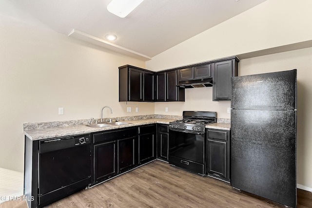 kitchen with light countertops, vaulted ceiling, a sink, under cabinet range hood, and black appliances