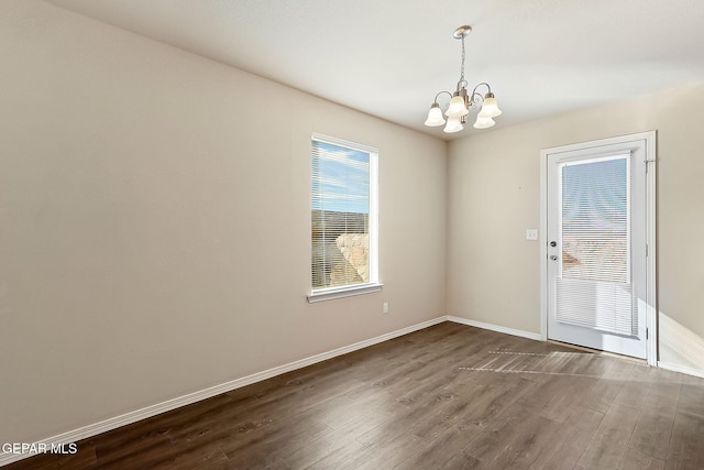 spare room featuring an inviting chandelier, baseboards, and wood finished floors