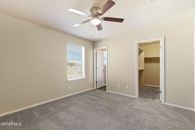 unfurnished bedroom with light carpet, a spacious closet, ceiling fan, and baseboards