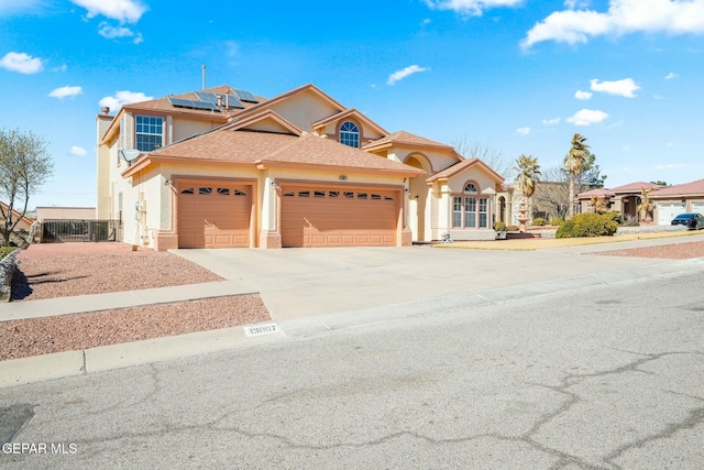 view of front facade with a garage, fence, concrete driveway, roof mounted solar panels, and stucco siding