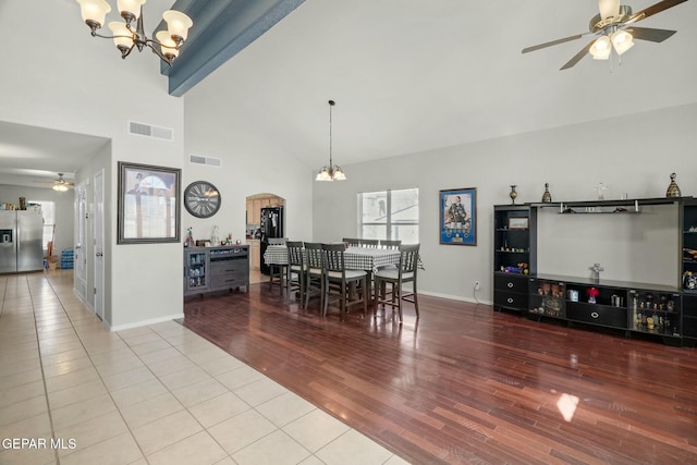 dining room with baseboards, visible vents, light wood-type flooring, high vaulted ceiling, and ceiling fan with notable chandelier