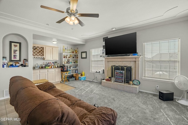 living room with visible vents, baseboards, a bar, a tiled fireplace, and crown molding