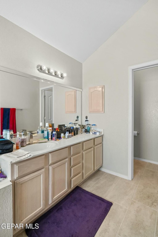 full bathroom featuring double vanity, baseboards, tile patterned floors, vaulted ceiling, and a sink