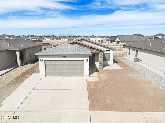 view of front of property with central AC unit, an attached garage, a shingled roof, concrete driveway, and a residential view