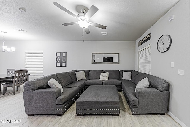 living area with light wood finished floors, visible vents, a textured ceiling, and ceiling fan with notable chandelier