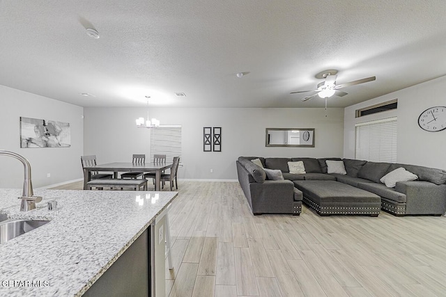 living room featuring light wood-style floors, baseboards, a textured ceiling, and ceiling fan with notable chandelier