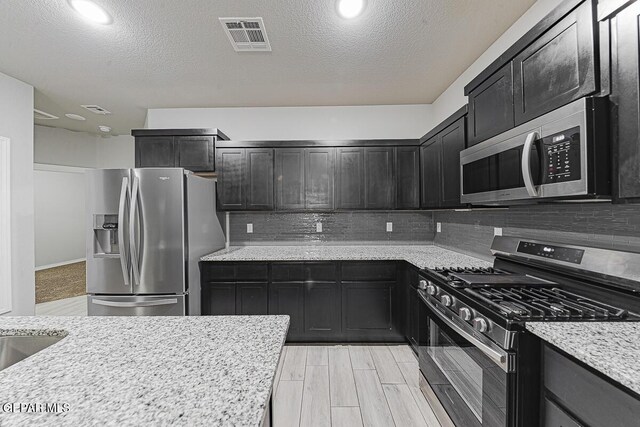 kitchen featuring tasteful backsplash, appliances with stainless steel finishes, visible vents, and light stone countertops