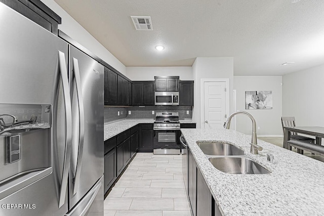 kitchen with visible vents, backsplash, appliances with stainless steel finishes, a sink, and dark cabinetry