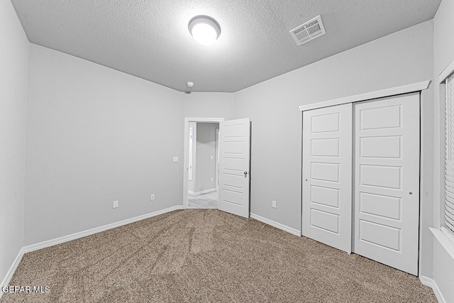 unfurnished bedroom with baseboards, visible vents, a textured ceiling, carpet flooring, and a closet