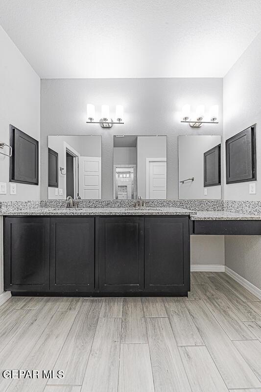 full bathroom featuring wood finished floors, a sink, baseboards, and double vanity