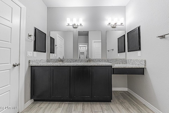 full bath with double vanity, wood finished floors, a sink, and baseboards