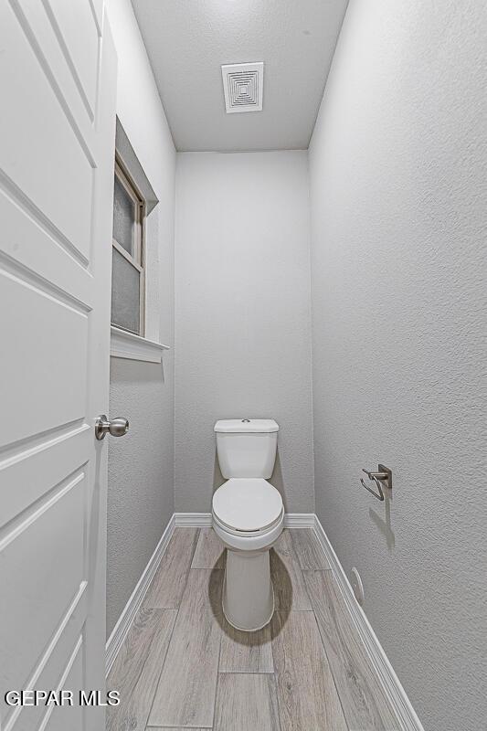 bathroom with wood finish floors, baseboards, and toilet