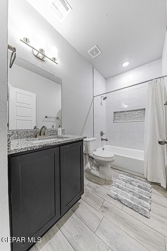 full bathroom featuring visible vents, toilet, shower / bathtub combination with curtain, and vanity