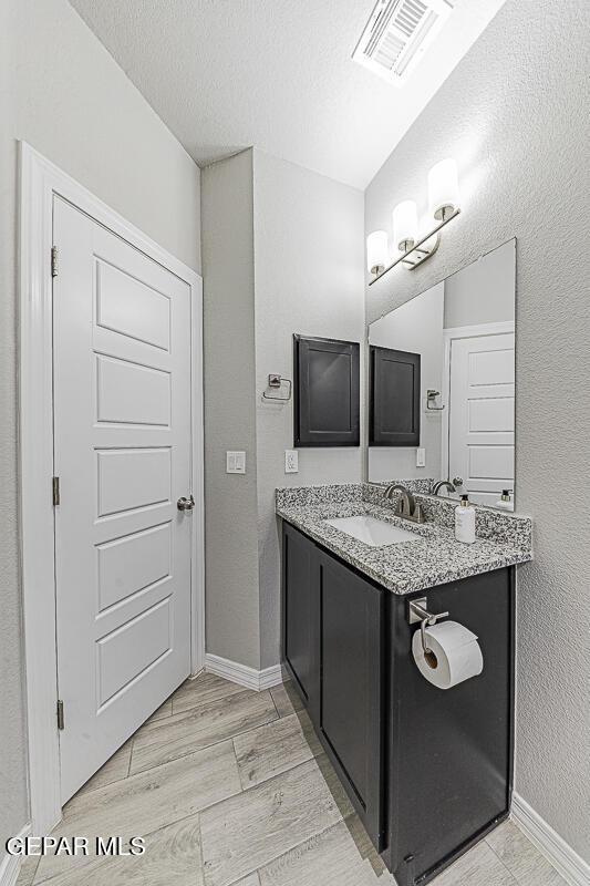 bathroom with a textured ceiling, wood finished floors, vanity, visible vents, and baseboards