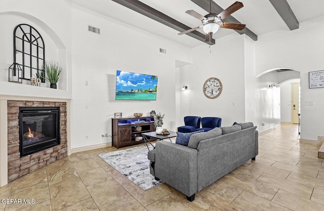 living area featuring arched walkways, beam ceiling, visible vents, a glass covered fireplace, and ceiling fan