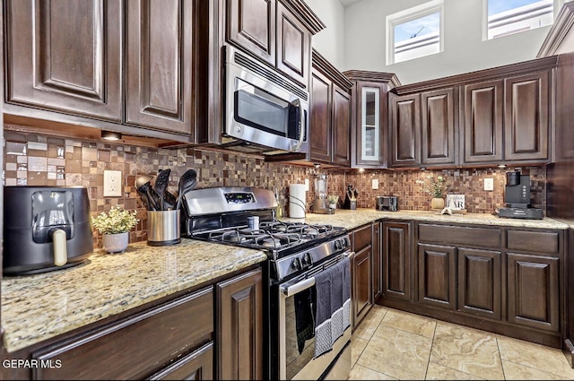 kitchen featuring light stone counters, appliances with stainless steel finishes, backsplash, and dark brown cabinetry