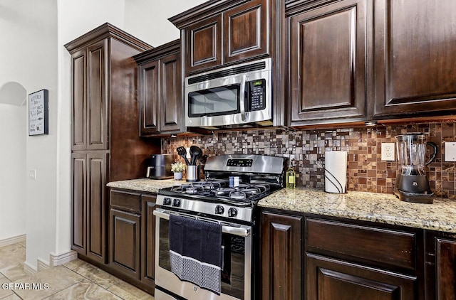 kitchen featuring dark brown cabinetry, appliances with stainless steel finishes, arched walkways, and backsplash