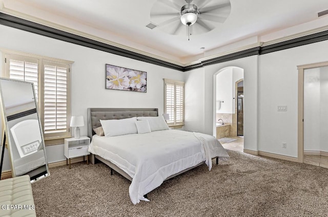 bedroom featuring arched walkways, connected bathroom, carpet floors, visible vents, and baseboards