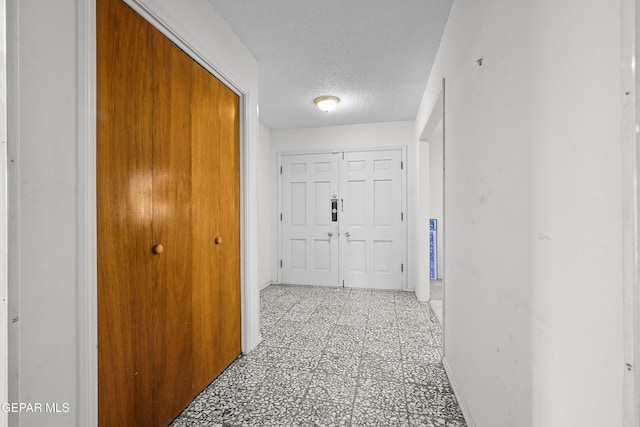 hall featuring light floors, baseboards, and a textured ceiling