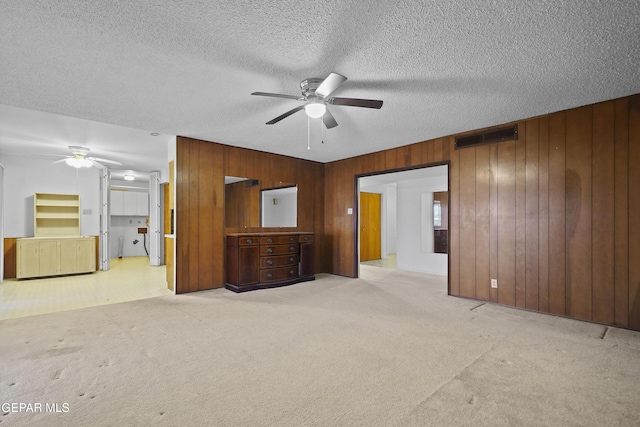 unfurnished living room with a ceiling fan, light colored carpet, visible vents, and wooden walls