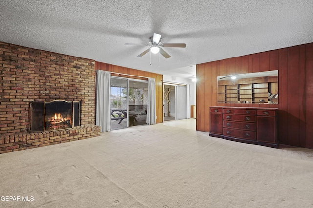 unfurnished living room with a textured ceiling, carpet, a fireplace, and wooden walls