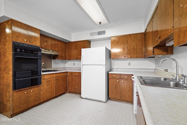 kitchen with under cabinet range hood, light countertops, a sink, and freestanding refrigerator