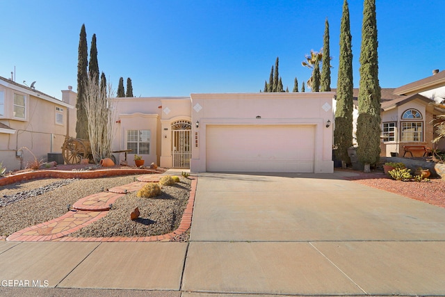 pueblo revival-style home with driveway, a garage, cooling unit, and stucco siding