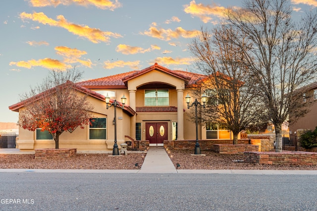 mediterranean / spanish house featuring a tiled roof, fence, and stucco siding