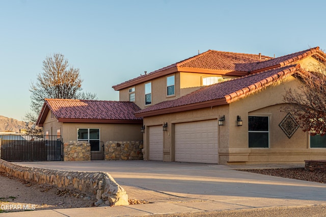 mediterranean / spanish-style home featuring concrete driveway, a tile roof, fence, and stucco siding