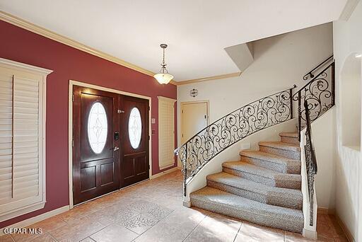 foyer entrance with crown molding, stairway, and baseboards