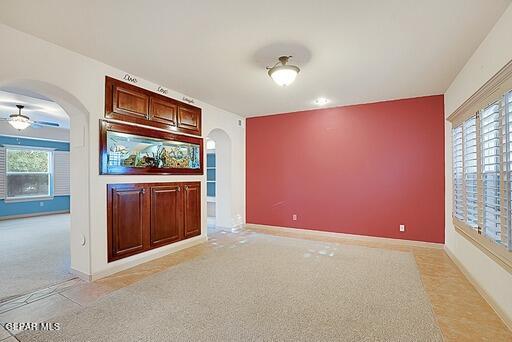 interior space featuring arched walkways, a healthy amount of sunlight, light colored carpet, and baseboards