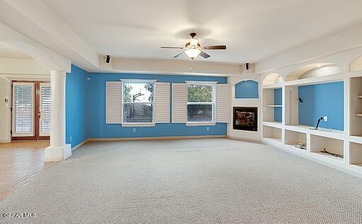 unfurnished living room with decorative columns, a ceiling fan, light colored carpet, built in shelves, and a fireplace